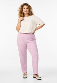 Kremowy top z krótkim rękawem w połączeniu z jasnoróżowymi spodniami. Spodnie mają prosty krój i elastyczny pas. Całość dopełniają czarno-białe buty.