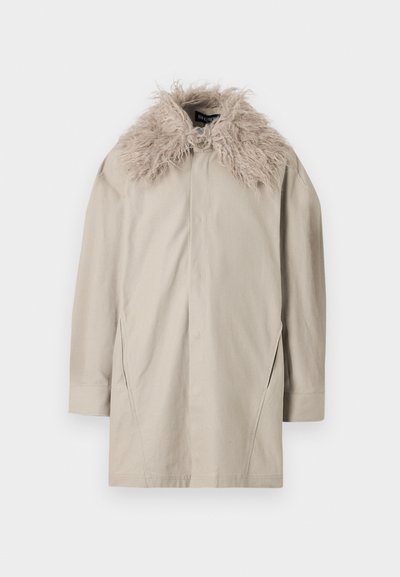 Beige långärmad kappa med stor fluffig pälskrage, knappstängning vid halsen och subtila sömdetaljer på framsidan och ärmarna.