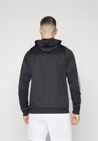 Svart hettegenser med en glatt tekstur, med snor i hetten og hvite striper langs ermene. Bakfra vises en tettsittende design og kant.