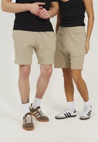 Shorts en velours côtelé beige jusqu'aux genoux avec texture côtelée, taille élastique et poches latérales, portés par deux modèles.