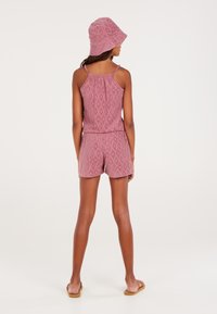 Mono corto rosa con estampado, tirantes delgados y cinturilla elástica, combinado con un gorro de cubo a juego. Las sandalias completan el conjunto.