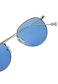 Gafas de sol aviador de metal con lentes azules, doble puente y almohadillas nasales transparentes. Montura delgada en tono plateado con forma de lente redondeada y elegante.