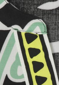 Kleurrijke stof met een zwarte basis en groene en witte abstracte patronen. Een gele accent met zwarte driehoekige vormen loopt langs de rand.