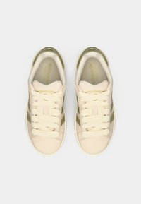 Μπεζ σουέντ αθλητικά παπούτσια Adidas με κρεμ κορδόνια και ελιάς πράσινες λεπτομέρειες, εμφανιζόμενα από πάνω σε λευκό φόντο.