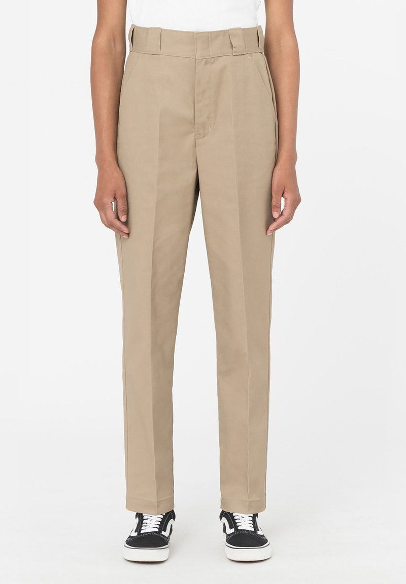 Béžové kalhoty s vysokým pasem a rovnými nohavicemi, s předními záševky a poutky na pás. Materiál má hladkou texturu. V kombinaci s černými teniskami.