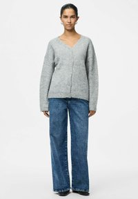 Sivi vuna kardigan s V-izrezom, zatvaranjem na dugmad i spuštenim ramenima. Uparen s trapericama s visokim strukom i širokim nogavicama u plavoj boji.