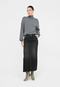 Grauer Rollkragenpullover, kombiniert mit einem schwarzen Denim-Maxikleid. Stiefel mit Schlangenprint und Absatz. Der Pullover hat lange Ärmel und eine lockere Passform.