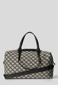 Sac en toile texturée avec une base beige et un motif logo noir répétitif, poignées en cuir noir et une sangle amovible pour plus de polyvalence.