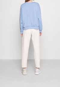 Ljusblå sweatshirt med sänkta axlar och ribbad nederkant, kombinerad med vita taperade byxor med två små bakfickor. Vita sneakers.