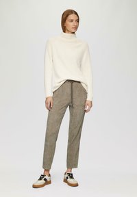 Crème ribbed coltrui, olijfgroene textuurbroek met trekkoord, en witte sneakers met zwarte accenten en tan-zolen.