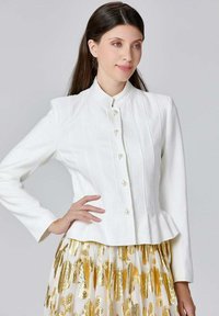Veste blanche structurée avec un col haut, devant à boutons et taille peplum. Le tissu a une finition texturée, rehaussée par une jupe accentuée de doré.