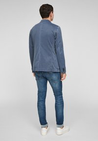Niebieski bawełniany żakiet o dopasowanym kroju, z dwoma bocznymi kieszeniami i zapinanymi mankietami, w połączeniu z ciemnymi dżinsami i białymi trampkami.