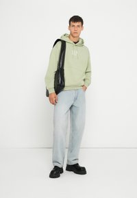 Felpa verde chiaro con logo "GAP", abbinata a jeans larghi blu chiaro e scarpe nere chunky. Borsa a spalla nera.
