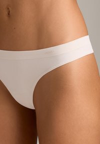 Nærbillede af en person iført hvidt sømløst bikiniundertøj, der viser hofte-, talje- og nederste maveområde.