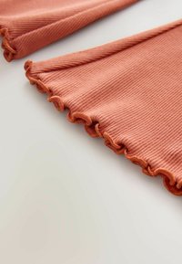 Bordázott pamutszövet tompa korallszínben, fodros széllel. Simaság érzete és puha esése, tiszta, hajtogatott kialakítást mutat.