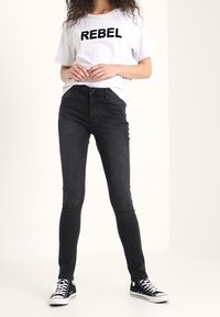 Jeans skinny negros combinados con una camiseta blanca que presenta un texto en relieve de "REBEL", complementados con zapatillas Converse negras.