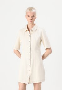 Robe chemise beige clair en tissu doux, dotée d'un col, de manches courtes et d'une fermeture à boutons à l'avant avec de grands boutons ronds.