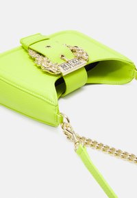 Mała limonkowo-zielona skórzana torebka na ramię z złotym łańcuszkiem i ozdobną złotą klamrą z logo Versace Jeans Couture.