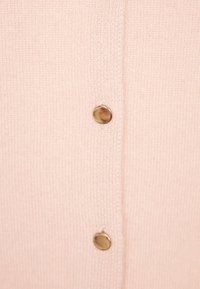 Ljusrosa kofta med ribbad textur, gyllene rundade knappar och en rak klippning med mittöppning.