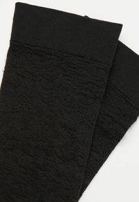 Schwarze knielange Socken mit dezentem floralen Jacquardmuster und einem einfarbigen schwarzen Bündchen auf weißem Hintergrund.