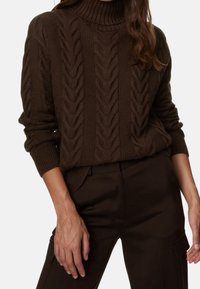 Brązowy sweter w splot kablowy z wysokim kołnierzem i ściągaczami, połączony z ciemnymi spodniami, prezentujący teksturowany, przytulny wzór.