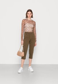 Blusa de mangas longas, transparente, com estampado de leopardo em tons de bege e castanho, combinada com calças cortadas em verde-oliva. Os acessórios incluem uma mala texturizada, de tom rosa claro.