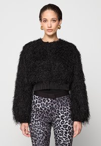 Giacca nera corta realizzata in materiale peloso con maniche larghe. Abbinata a pantaloni a vita alta con stampa leopardata e fascia elastica nera in vita.