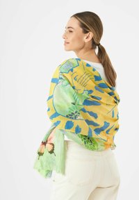 Écharpe multicolore avec des motifs jaunes et bleus, des dessins floraux et une accentuation de papillon. Tissu léger et texturé drapé sur les épaules.