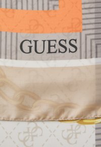 Silkescarf med en orange grafik, grå ränder och beige bakgrund. Anmärkningsvärd "GUESS"-logotyp med kedjemönsterdetalj längs kanten.