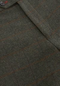 Tissu en laine verte avec de fines lignes à carreaux rouges, comprenant un bouton et un détail de rabat, suggérant une poche ou une partie de vêtement.