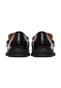Paire de chaussures habillées en cuir noir à talons bas, vues de dos sur un fond blanc.