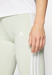 Svetlo zelene legice z belimi tristripnimi detajli, z belim Adidasovim logotipom. Gladek, elastičen material povečuje udobje.