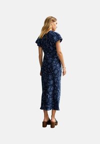 Robe bleu foncé avec un corsage ajusté et une jupe fluide. Présente un design de manche à volants et un motif graphique bleu clair répétitif.
