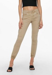 Pantalones cargo beige con corte ajustado, puños elásticos y bolsillos laterales. Fabricados en una tela suave, con detalles de costura que ofrecen un aspecto cuidado.
