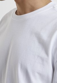 White cotton t-shirt with a crew neckline, smooth texture, and short sleeves. Stitched seams visible along the neckline and shoulder.
