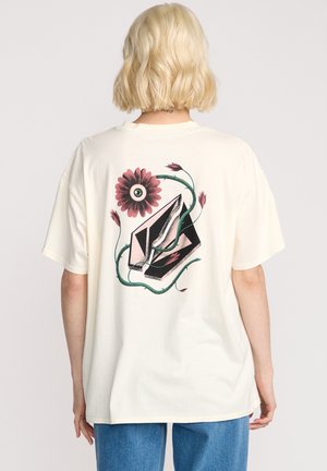 Cream cotton t-shirt featuring a colorful graphic of an eye surrounded by flowers and leaves on the back. Relaxed fit, short sleeves.