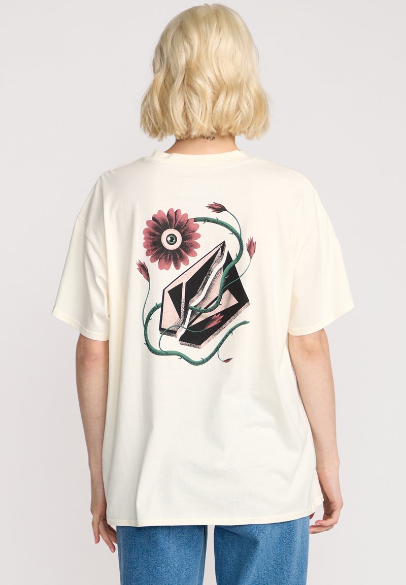 T-shirt en coton crème avec un graphique coloré d'un œil entouré de fleurs et de feuilles au dos. Coupe décontractée, manches courtes.