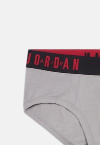 Γκρι ανδρικά εσώρουχα με μαύρη ζώνη, η οποία φέρει κόκκινο κείμενο "JORDAN" και ορατά ραφάκια κατά μήκος του ανοίγματος του ποδιού και του μπροστινού πάνελ.