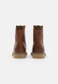 Brune lær ankle boots med en teksturert finish, kontrasterende semsket krage og en naturlig gummisåle. Bakvisning viser sydd detalj og logo.