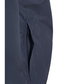 Tessuto della giacca navy con un primo piano di una tasca con zip sul lato sinistro, caratterizzata da bordi cuciti e una texture liscia e opaca.