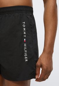 Μαύρα μαγιό σορτς από ελαφρύ ύφασμα. Διαθέτουν ελαστική μέση και λευκό κεντημένο λογότυπο «TOMMY HILFIGER» με χρωματικές λεπτομέρειες.