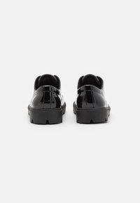 Schwarze Lackleder-Sneaker mit runder Zehenpartie, Gummisohle und minimaler Nahtführung. Der Absatz ist leicht erhöht und hat eine strukturierte Oberfläche.