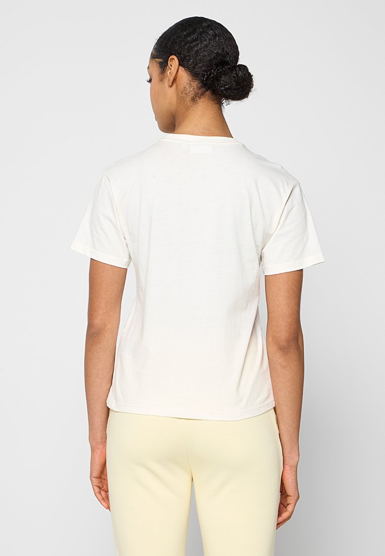 Weißes Baumwoll-T-Shirt, kurze Ärmel, klassisches Rundhalsausschnitt-Design. Weiche Textur mit einem eingenähten Etikett auf der Rückseite. Kombiniert mit hellgelben Hosen.