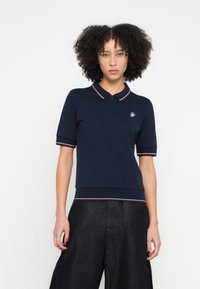 Sötétkék galléros póló cipzáras nyakkivágással és rövid ujjakkal, kontrasztos csíkos díszítéssel és kis hímzett logóval a mellrészen.