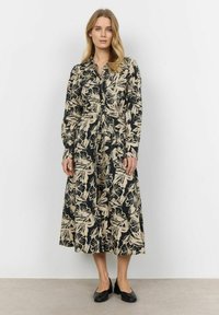 Lange zwarte jurk met crèmekleurig bloemenpatroon, knoopsluiting aan de voorkant, kraag en lange mouwen. Gepaard met zwarte ballerina's.