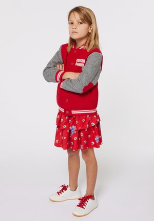 Rode varsity jack met grijze mouwen, borduursel "KENZO PARIS", gelaagde rode bloemenruffle jurk en witte sneakers met rode veters.