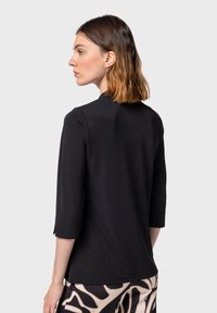 Top nero aderente con maniche a 3/4 e scollatura rotonda. Tessuto morbido con una leggera lucentezza. Indossato con pantaloni a fantasia con disegni audaci.