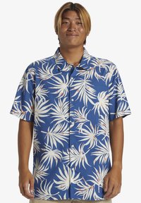 Camisa de manga corta con botones en tela azul con un patrón de hojas de palma blancas y detalles en rosa claro. Presenta un collar puntiagudo y botones en la parte delantera.