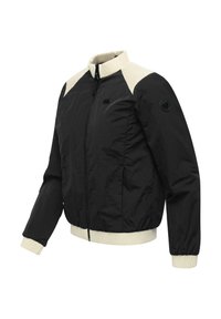 Veste noire à fermeture éclair avec col côtelé crème, panneaux d'épaule, poignets et ourlet, ornée d'un patch circulaire sur la manche gauche.