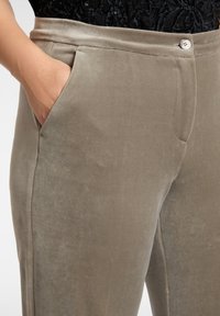 Pantaloni in velluto di colore verde oliva tenue, con una texture liscia, tasche laterali e chiusura in vita con bottoni.